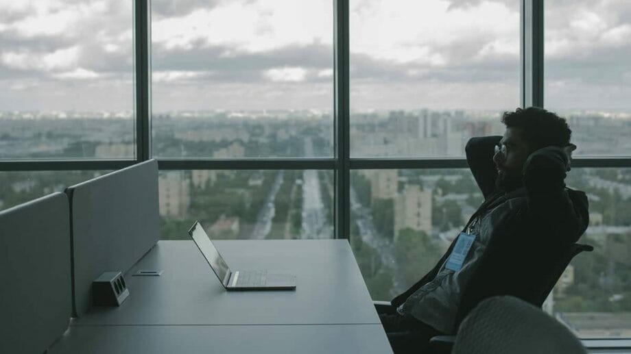 A man sitting at a desk with a laptop in front of a window.