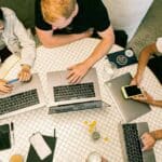 A group of people sitting around a table with laptops.