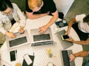 A group of people sitting around a table with laptops.