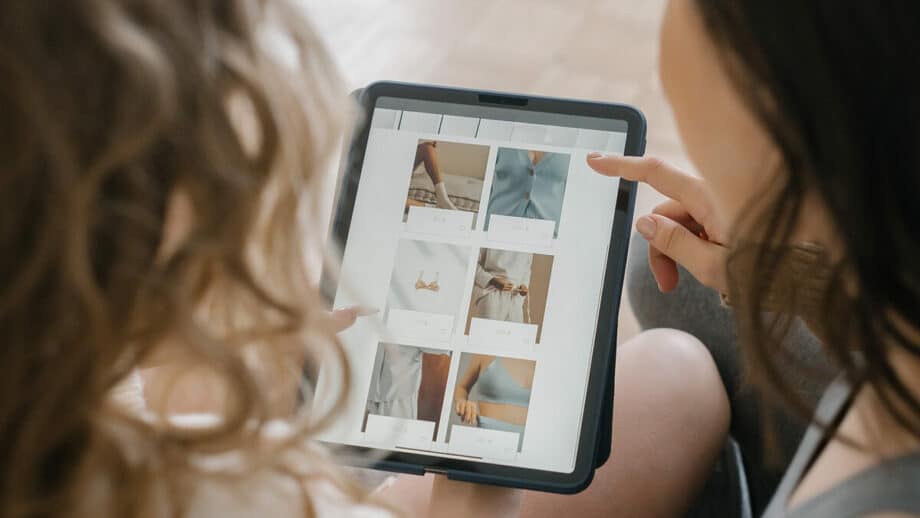 A woman is looking at a tablet with clothes on it.