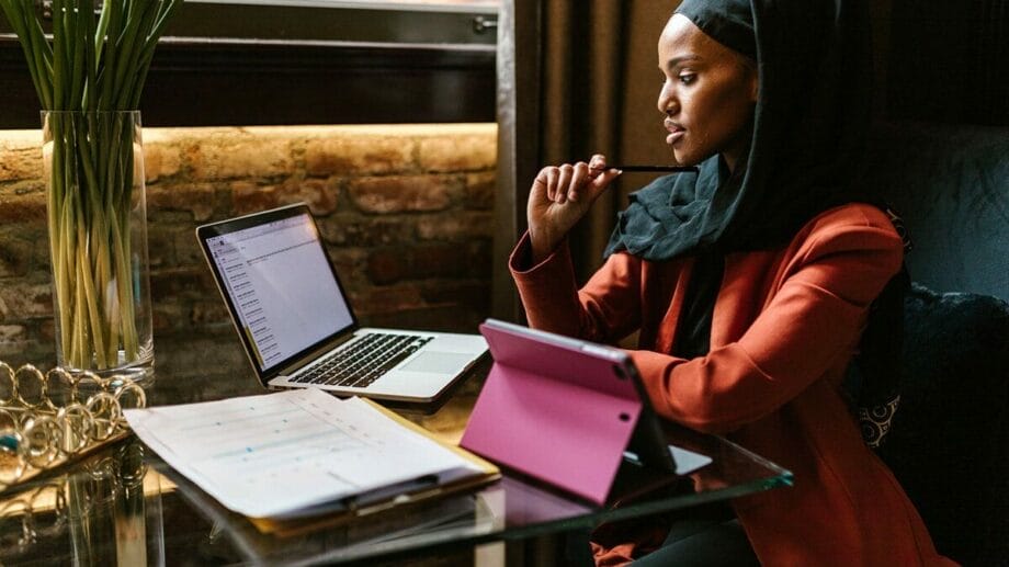 A woman wearing a hijab sitting at a table with a laptop.