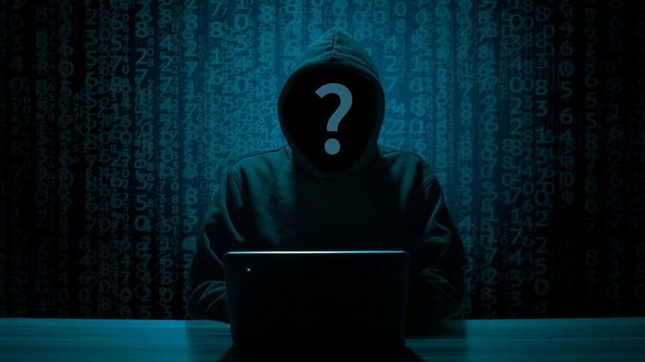 A hooded figure at a laptop with a question mark over their face, set against a backdrop of digital numbers.