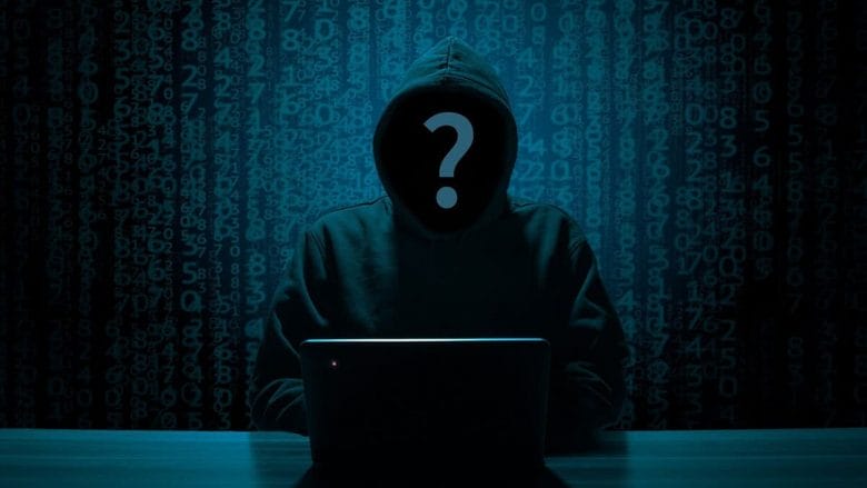 A hooded figure at a laptop with a question mark over their face, set against a backdrop of digital numbers.