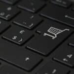 Close-up of a black computer keyboard with a focus on a key featuring a shopping cart icon, symbolizing online shopping, surrounded by other keys including pound and home keys.
