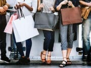Four individuals standing in a line, holding various shopping bags. They are dressed in casual attire, and their faces are not visible.