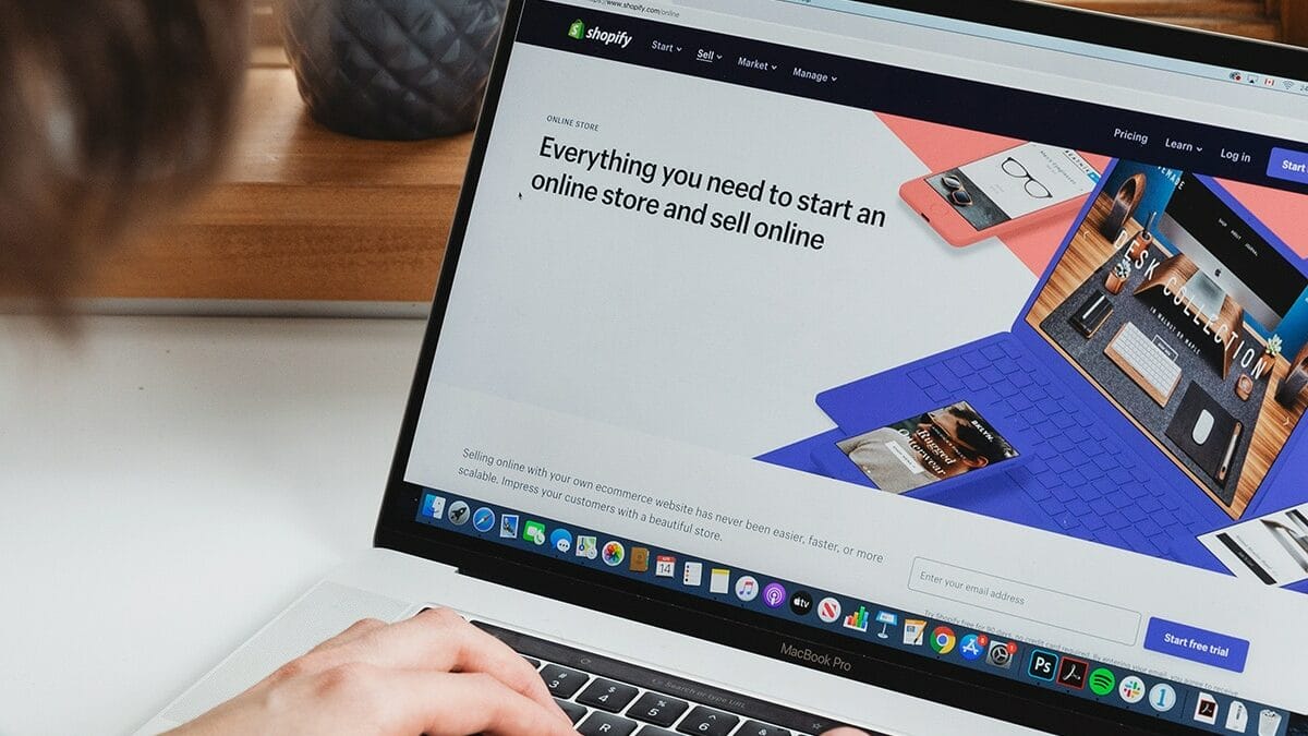 A person using a laptop with the Shopify website open, displaying information on starting an online store and selling products digitally.