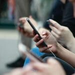 Close-up of multiple people using smartphones while sitting in a row, focusing on hands and phones.