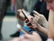 Close-up of multiple people using smartphones while sitting in a row, focusing on hands and phones.