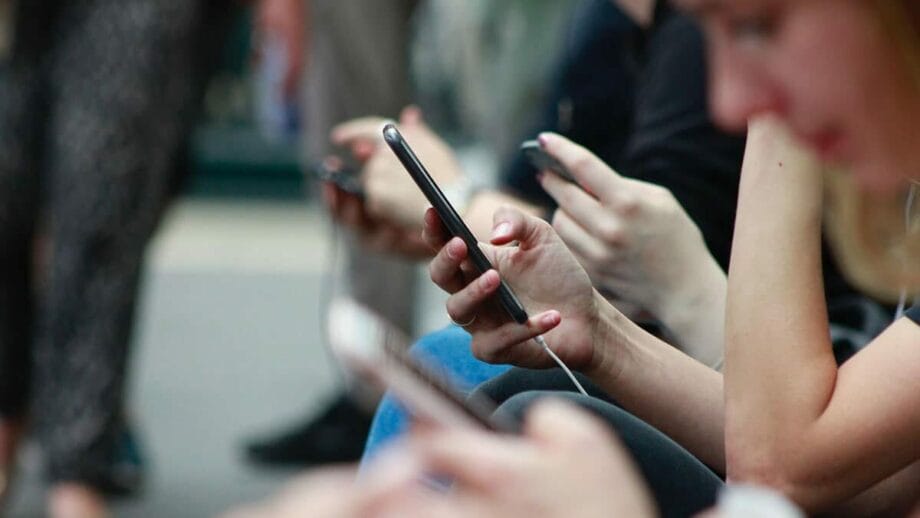 Close-up of multiple people using smartphones while sitting in a row, focusing on hands and phones.
