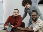Three men are sitting at a table with a laptop in front of them.