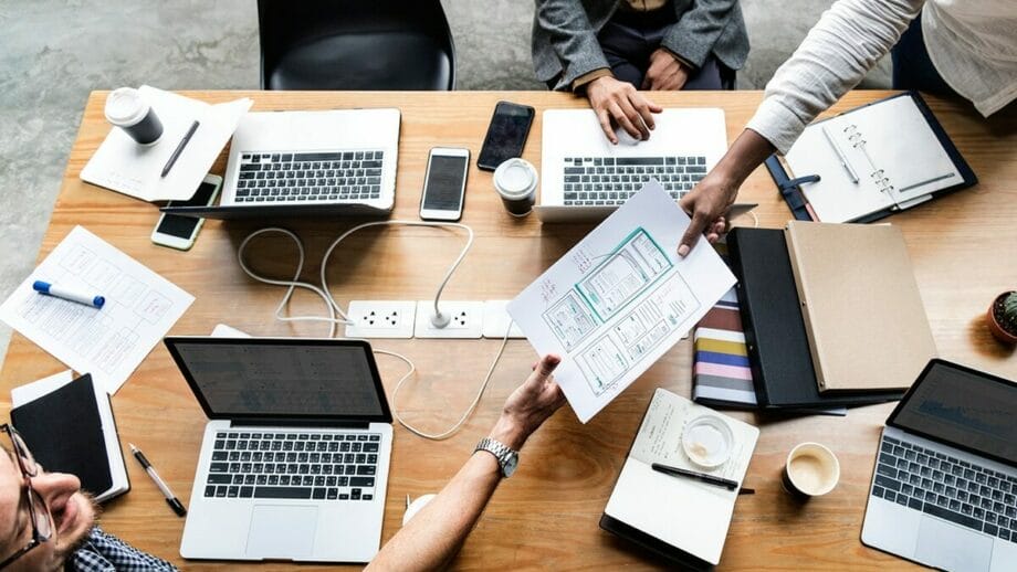 A group of mobile app developers sitting around a table with laptops and papers.