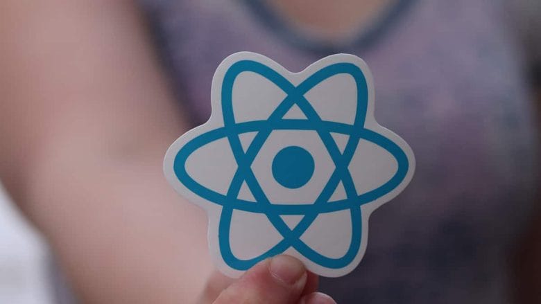 A woman is holding up a sticker with the react logo on it.