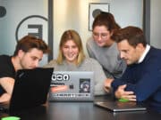 A group of people sitting around a table looking at a laptop.