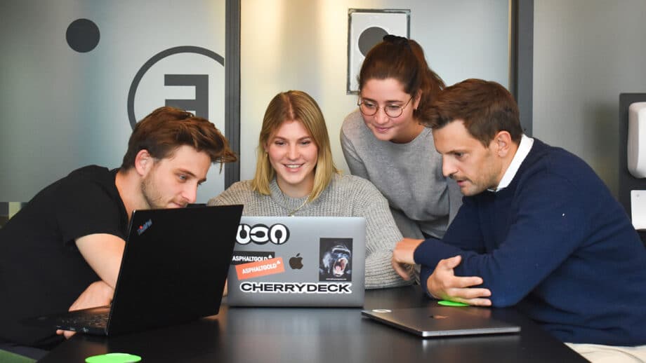 A group of people sitting around a table looking at a laptop.