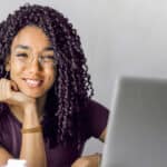 A woman with curly hair sitting at a desk with a laptop.