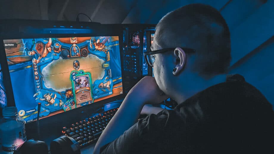 A person is playing a colorful card-based video game on a computer in a room with blue ambient lighting.