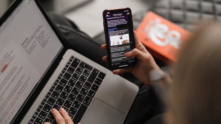 A woman is using a smartphone while sitting at a laptop.