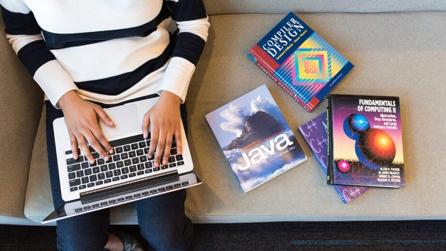 A woman sitting on a couch with a laptop and books.