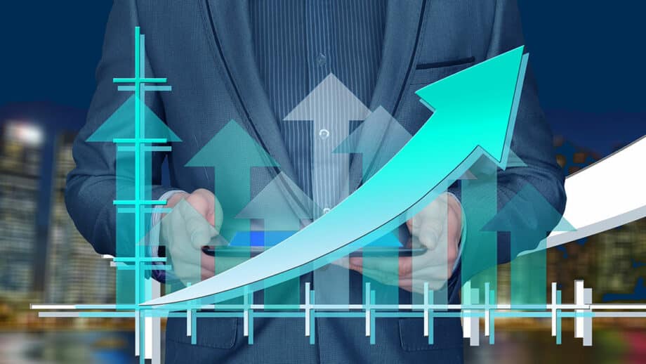 Man in suit holding device with upward arrows and bar graphs, symbolizing growth or progress, over a blurred cityscape background.