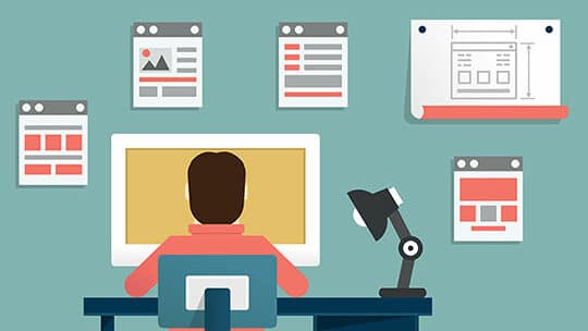 A graphic designer working at a desktop computer with various web design layouts on the wall.