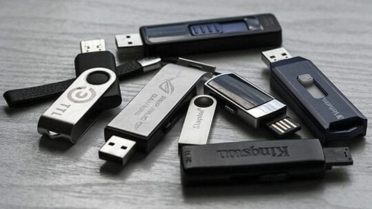 A collection of various USB flash drives is scattered on a light wooden surface.