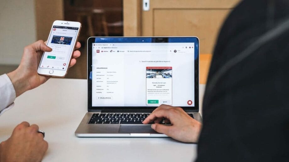 Two people using a laptop and a cell phone to view a website.