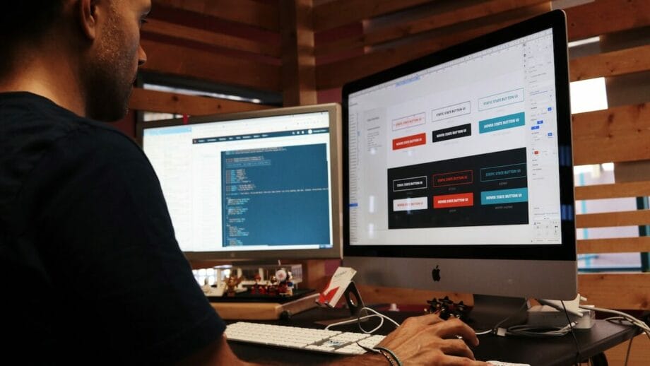 A man developing a website by sitting at a desk with two monitors in front of him.