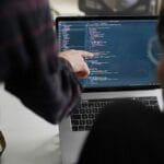 Two people working on a laptop with code on it.