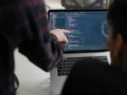 Two people working on a laptop with code on it.