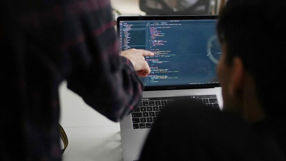 Two people working on a laptop with code on it.