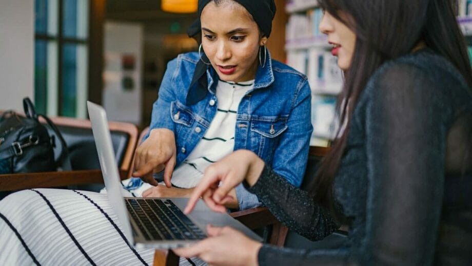 Two women looking at a laptop in a library.