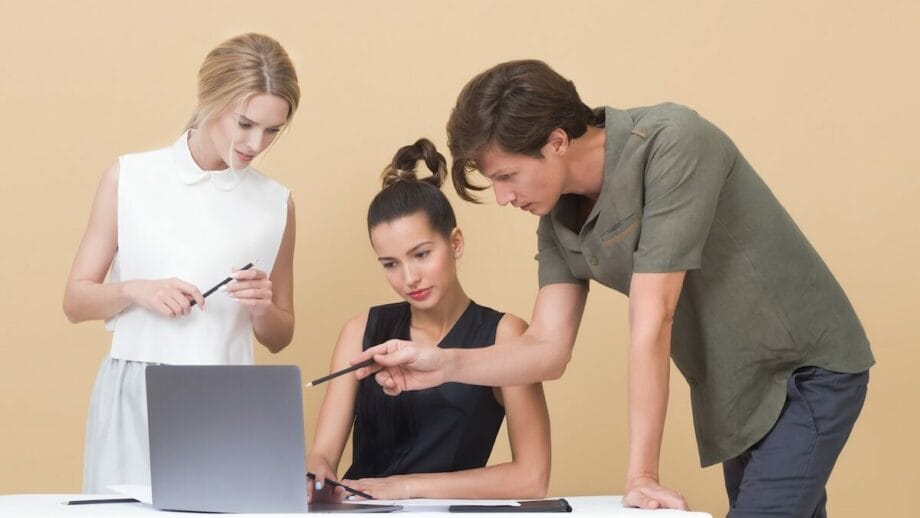 Three business people looking at a laptop on a beige background.