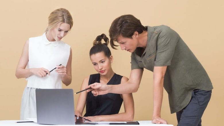 Three business people looking at a laptop on a beige background.