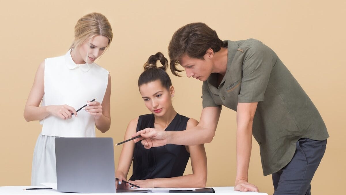 Three business people looking at a laptop on a beige background.