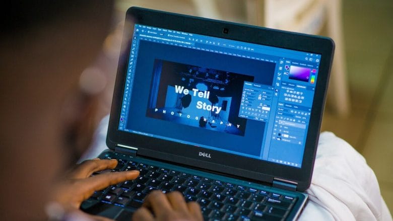 A person is using a dell laptop with an image editing application open, working on a project with the text "we tell story" visible on the screen.