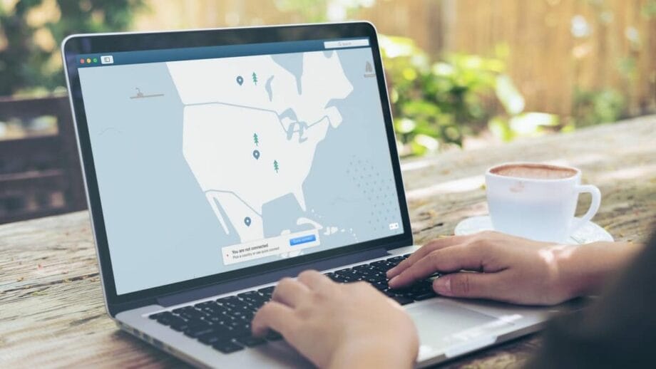 A person using a laptop outdoors with a map interface open on the screen and a cup of coffee nearby.