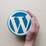A person holding a wordpress logo on top of a wooden table.