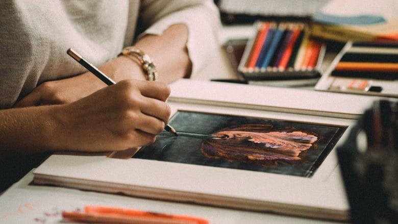 A woman is drawing a flower on a piece of paper.