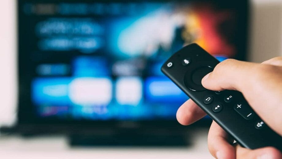 A person holding a remote control in front of a tv.