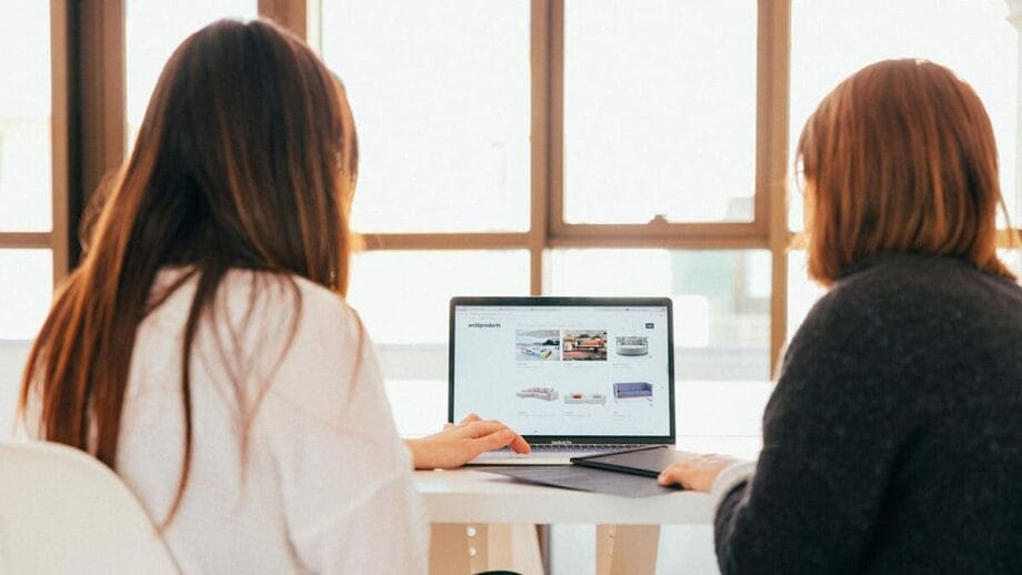 Two women sitting at a table looking at a laptop.