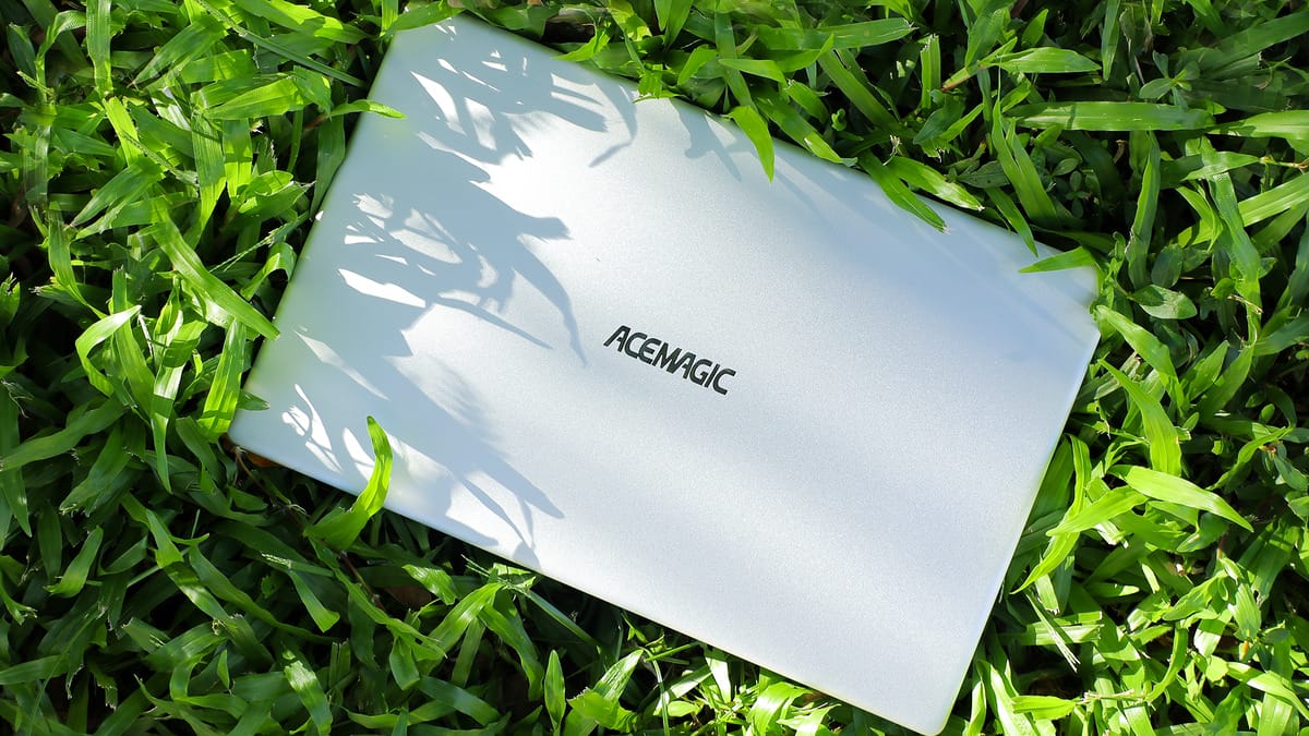 A white ACEMAGIC ‎AX15 Laptop laying in the grass.