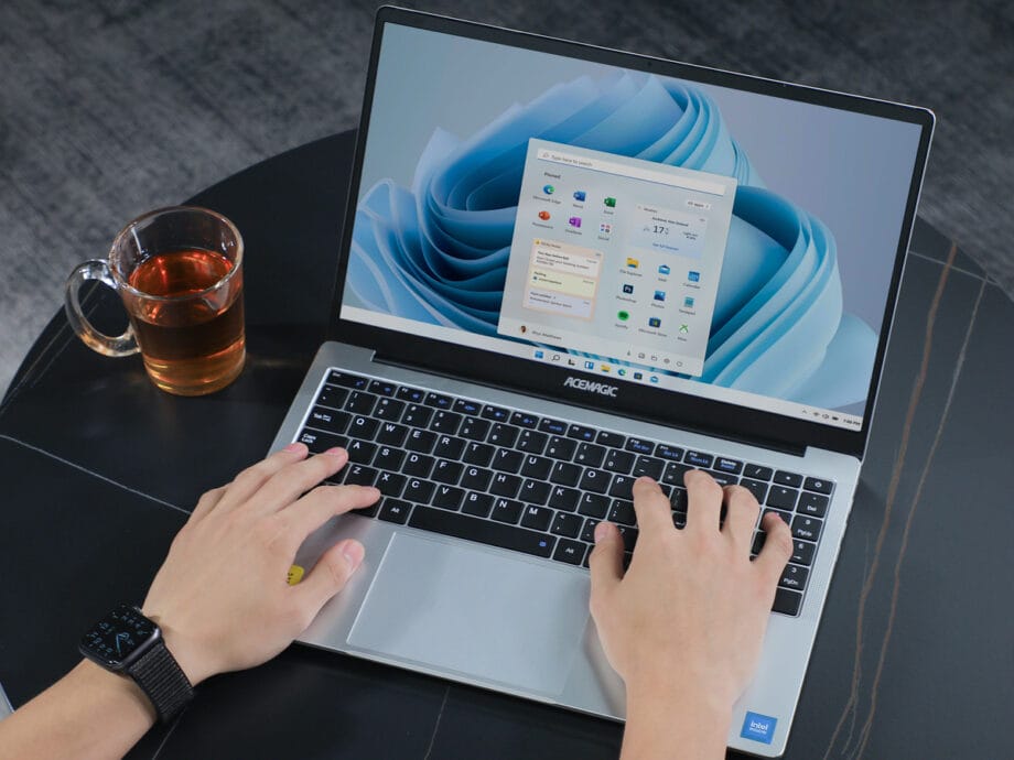 A person using an ACEMAGIC ‎AX15 Laptop on a table with a cup of coffee.