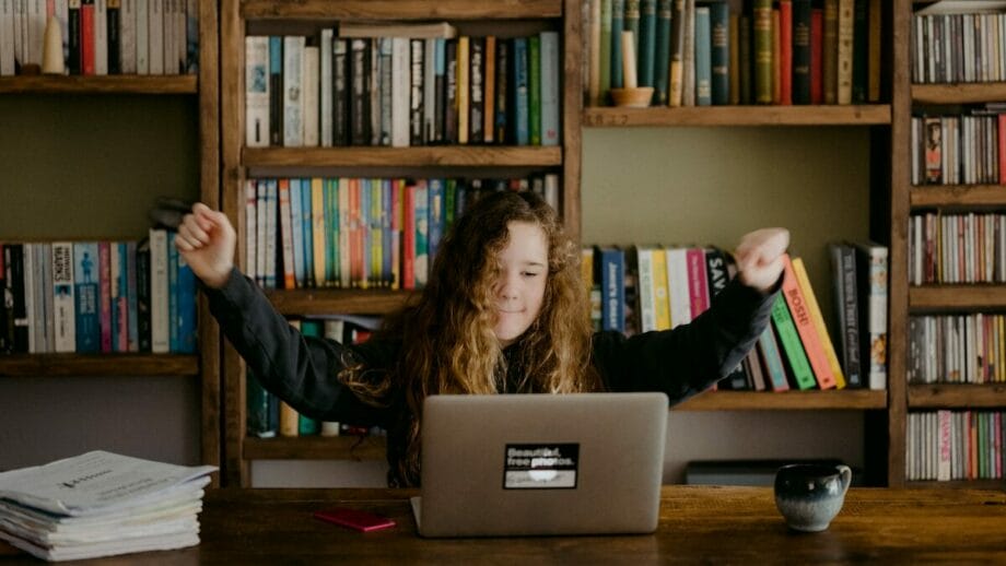 A woman is sitting at a desk with a laptop in front of a bookcase.