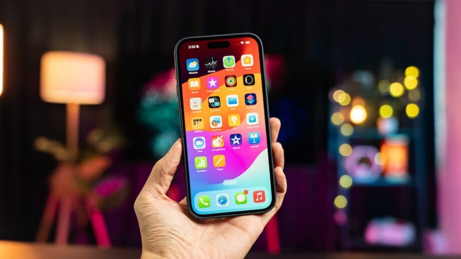 A person is holding up an iPhone 15 Pro Max with a lot of apps on it.