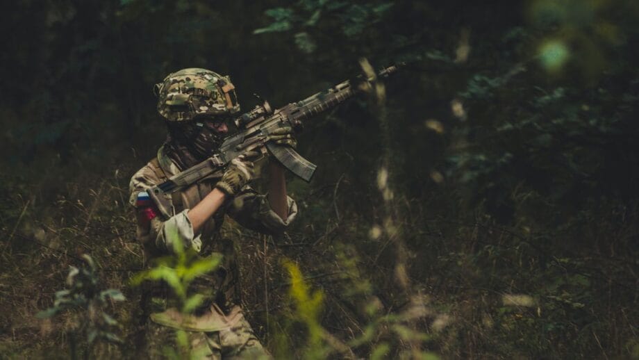 A soldier in camouflage is holding a rifle in the woods.