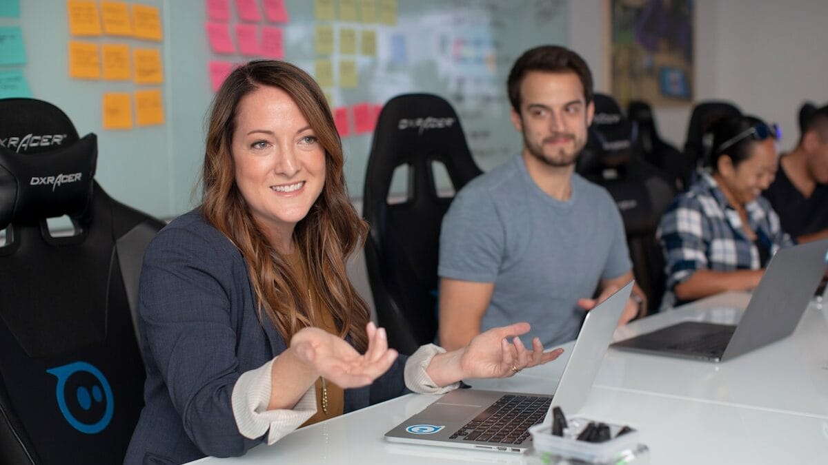 A group of people sitting at a desk with laptops in front of them.