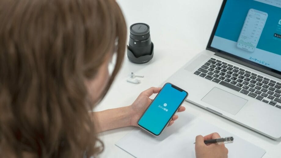 A woman using her phone and laptop at a desk.
