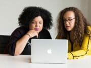 two women looking at the screen of a MacBook