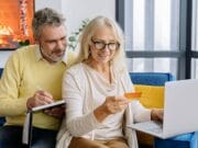 A couple sitting on a couch with a laptop and a credit card.