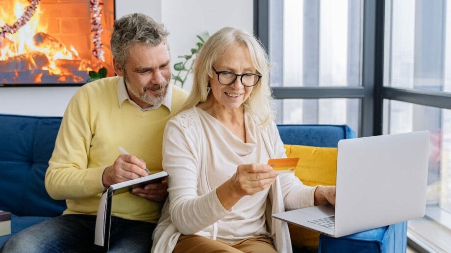 A couple sitting on a couch with a laptop and a credit card.